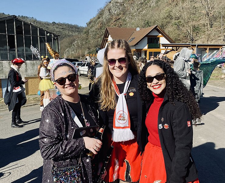 Drei fröhliche Frauen in Kostümen feiern den Rosenmontagszug in Altenahr-Altenburg bei strahlendem Sonnenschein.