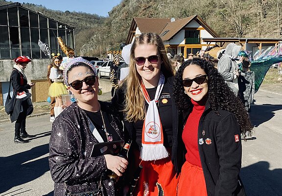 Drei fröhliche Frauen in Kostümen feiern den Rosenmontagszug in Altenahr-Altenburg bei strahlendem Sonnenschein.
