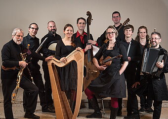 Eine 10 Köpfige Bänd mit diversen Blas-, Seiten-, und Sonstigen- Instrumenten alle in Schwarz gekleidet.