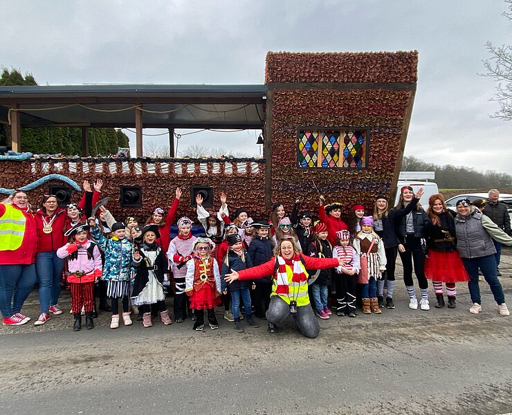 Aufstellung von als Piraten verkleideten Kindern und Erwachsenen von einem Karnevalsumzugswagen der aussieht wie ein Schiff