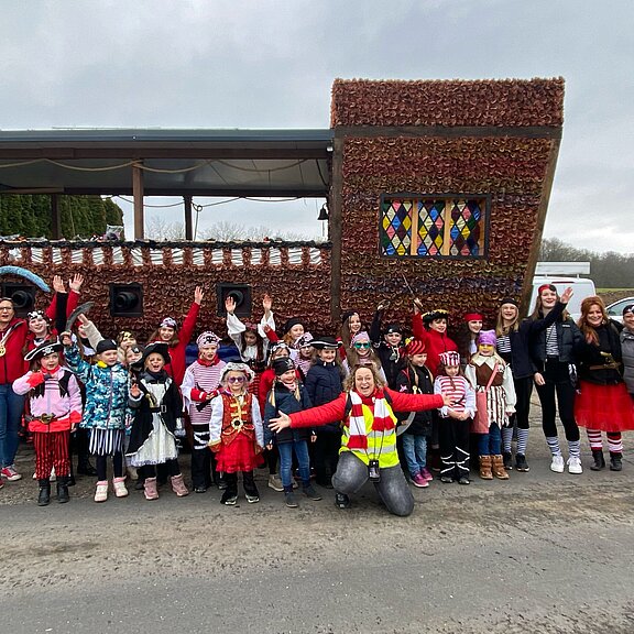 Aufstellung von als Piraten verkleideten Kindern und Erwachsenen von einem Karnevalsumzugswagen der aussieht wie ein Schiff